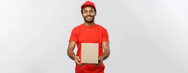 Conceito de entrega - Retrato de homem de entrega afro-americano feliz em pano vermelho segurando um pacote de caixa. Isolado no estúdio Grey Background. Espaço de cópia . — Fotografia de Stock