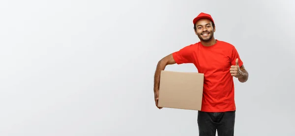 Conceito de entrega - Retrato de homem de entrega afro-americano feliz segurando um pacote de caixa e mostrando thumps para cima. Isolado no estúdio Grey Background. Espaço de cópia . — Fotografia de Stock
