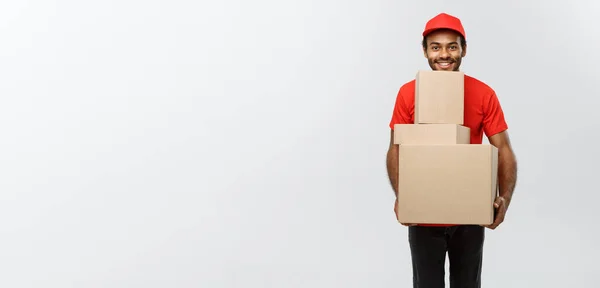 Conceito de entrega - Retrato de homem de entrega afro-americano feliz em pano vermelho segurando um pacote de caixa. Isolado no estúdio Grey Background. Espaço de cópia . — Fotografia de Stock