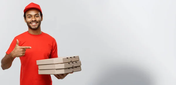 Concetto di consegna Ritratto dell'uomo di consegna afroamericano felice che punta la mano per presentare pacchetti di scatole di pizza. Isolato su sfondo grigio studio. Copia spazio . — Foto Stock