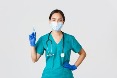 Covid-19, koronavirüs hastalığı, sağlık çalışanları konsepti. Kendine güvenen Asyalı kadın hemşire, tıbbi maskeli doktor ve lastik eldivenli, aşılı şırınga tutan, beyaz arka planda duran