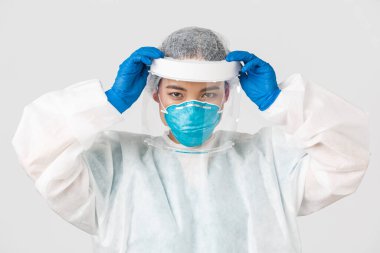 Covid-19, koronavirüs hastalığı, sağlık çalışanları konsepti. Ciddi görünümlü Asyalı kadın doktor, bulaşıcı bölgeye girmeden önce yüz kalkanı ve kişisel koruyucu ekipman takın.