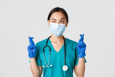 Covid-19, koronavirüs hastalığı, sağlık çalışanları konsepti. Umut dolu Asyalı doktor. Maskeli ve eldivenli. Sol üst köşeye bakıyor ve dua ediyor.