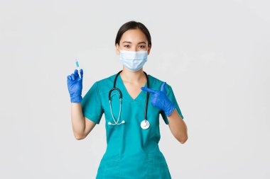 Covid-19, koronavirüs hastalığı, sağlık çalışanları konsepti. Dost canlısı Asyalı kadın doktor, tıbbi maskeli doktor ve şırıngayı aşıyla gösteren önlük.