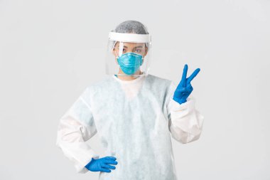 Covid-19, koronavirüs hastalığı, sağlık çalışanları konsepti. Küstah Asyalı kadın doktor, doktor ya da teknoloji laboratuarı kişisel koruma ekipmanları barış işareti gösteriyor, beyaz arka plan