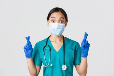 Covid-19, koronavirüs hastalığı, sağlık çalışanları konsepti. Heyecanlı ve umut dolu Asyalı doktor, sağlık maskeli hemşire ve lastik eldiven şans dileyin, dileğinizi gerçekleştirin, beyaz arka plan