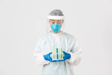 Covid-19, koronavirüs hastalığı, sağlık çalışanları konsepti. Heyecanlı Asyalı kadın doktor, kişisel koruyucu ekipman teknolojisi laboratuarı aşı ya da analizlerle dolu test tüpleri, beyaz arka plan.