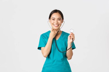 Covid-19, sağlık çalışanları ve virüs konseptini önlemek. Neşeli gülümseyen Asyalı kadın doktor, doktor hastaya danışıyor, steteskoplu, ayakta duran beyaz arka planı olan birini muayene ediyor.