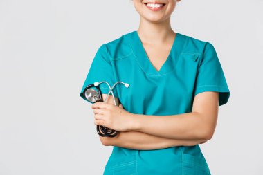 Covid-19, koronavirüs hastalığı, sağlık çalışanları konsepti. Asyalı kadın doktor vücudu gülümsüyor, kollar çapraz göğüste kendinden emin ve steteskop tutuyor, beyaz arka planda duruyor.