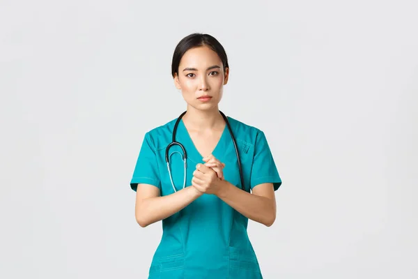 Covid-19, zdravotníci, pandemický koncept. Naděje vážně vypadající asijské zdravotní sestra, lékař žádá něco s ustaraným obličejem, sevřít ruce k sobě na podporu během coronavirus, bílé pozadí — Stock fotografie
