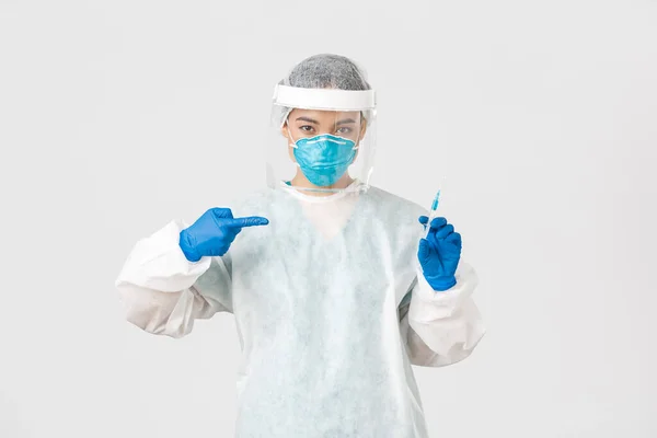 Covid-19, coronavirus disease, healthcare workers concept.严重的亚洲女医生，PPE个人防护设备的医生，手指指向装有疫苗的注射器，白色背景 — 图库照片