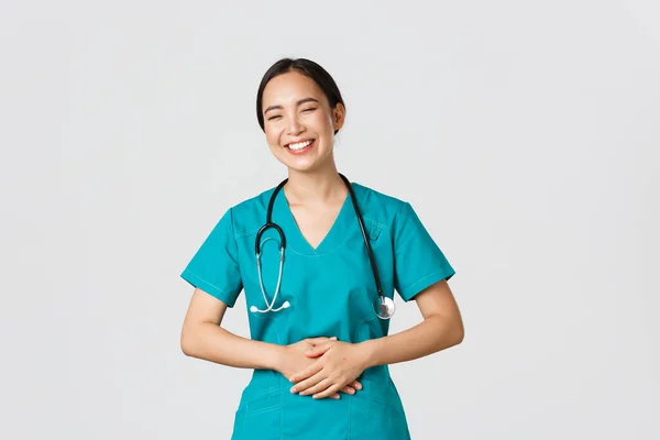 Covid-19, zdravotníci, pandemický koncept. Šťastný pěkný asijský žena lékař, lékař v drhnutí baví, směje se a dotýká břicha při vtipkování kolem s nemocničním personálem — Stock fotografie