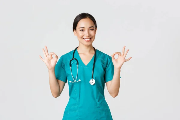 Covid-19, zdravotníci, pandemický koncept. Profesionální sebevědomý asijské žena lékař, stážista v čistírně ujišťují pacienty vše dobré, ukazuje v pořádku gesto spokojen, s úsměvem potěšen — Stock fotografie