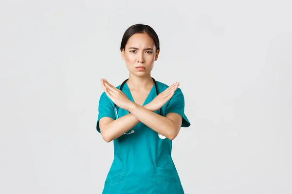Covid-19, zdravotníci, pandemický koncept. Znepokojený vážně vypadající asijské ženy lékař ukázat křížové gesto, chcete zastavit, zakázat nebo zakázat nebezpečné akce, bílé pozadí — Stock fotografie