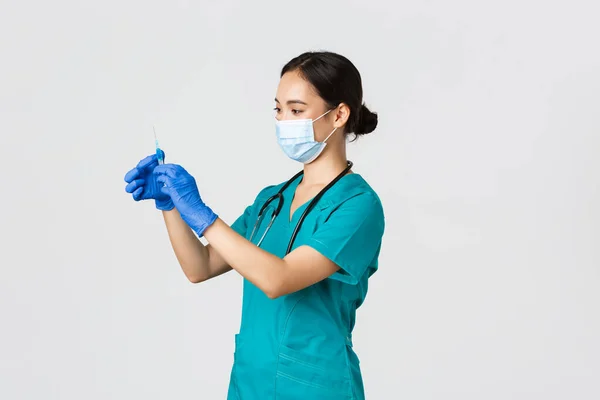 Covid-19, coronavirus disease, healthcare workers concept. Profile of asian female doctor, nurse in medical mask and globes, fill syringe with vaccine, doing vaccination shots, white background — Stock Photo, Image