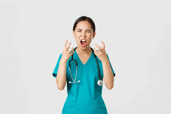 Covid-19, healthcare workers and preventing virus concept. Angry pissed-off asian female nurse, doctor losing temper, stressed-out physician shouting in anger, looking mad and aggressive — Foto Stock