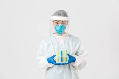 Covid-19, koronavirüs hastalığı, sağlık çalışanları konsepti. Şaşırmış Asyalı kadın doktor, kişisel koruyucu ekipman teknolojisi laboratuarı aşı ya da analizlerle dolu test tüpleri, beyaz arka plan.
