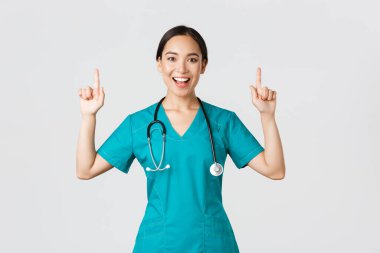 Covid-19, sağlık çalışanları, salgın konsepti. Gülümseyen güzel hemşire, doktor ya da doktor ya da stajyer doktor. Parmakla işaret ediyor, afişi gösteriyor, duyuru yapıyor, reklam yapıyor.