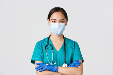 Covid-19, koronavirüs hastalığı, sağlık çalışanları konsepti. Kendine güvenen, gülümseyen, profesyonel Asyalı doktor, tıbbi maskeli hemşire ve lastik eldivenler muayene için hazır, beyaz arka plan.