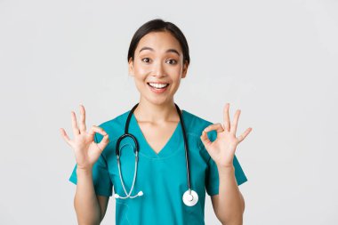 Sağlık çalışanları, virüsü önleme, karantina kampanyası konsepti. Heyecanlı ve memnun Asyalı kadın doktor, steteskoplu hemşire, iyi niyet göstergesi, beyaz arka plan.