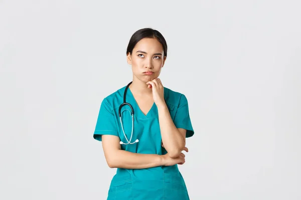 Covid-19, pracownicy służby zdrowia, koncepcja pandemii. Zdenerwowana i zaniepokojona azjatycka lekarka, pielęgniarka na dyżurze wyglądająca na podrażnioną lub zmęczoną, przewracanie oczami znudzona i wydychająca, stojąca na białym tle w fartuchu — Zdjęcie stockowe