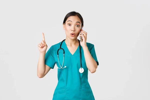 Covid-19 、医療従事者とウイルスの概念を防止します。美しいアジアの女性の医者の肖像,電話で話す頭皮の看護師と偉大なアイデアを持っているとして指を上げる,覚えています。 — ストック写真