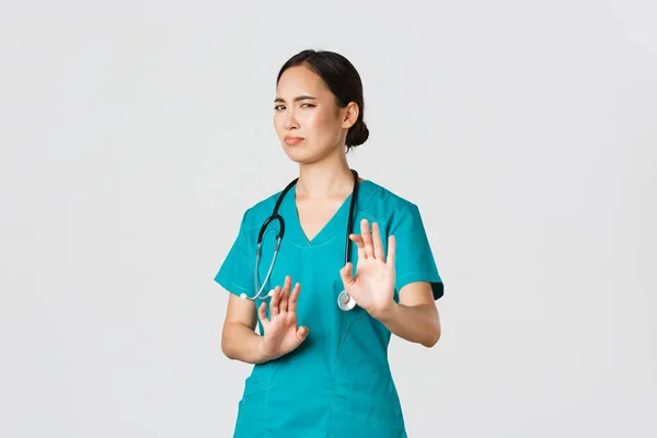Covid-19, pracownicy służby zdrowia, koncepcja pandemii. Niechętna zabawna azjatycka pielęgniarka, lekarz unikający kogoś, odsuń się i pokaż stop gest, grymaszenie lub żar jako odrzucenie okropnej oferty, odrzuć — Zdjęcie stockowe