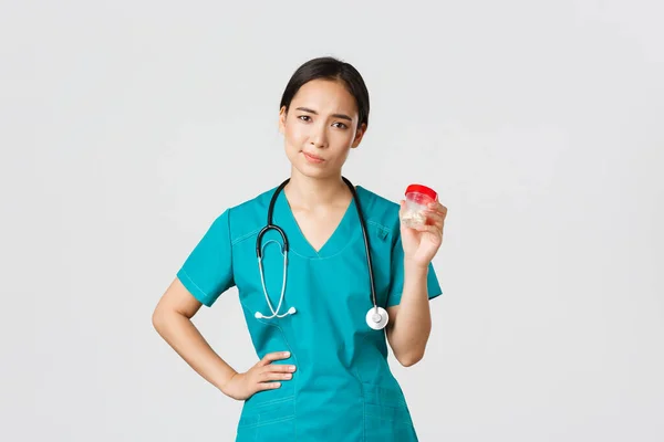 Zdravotničtí pracovníci, prevence viru, koncepce karanténní kampaně. Skeptické a nespokojené asijské ženské lékaře, zdravotní sestra nedoporučují léky, úšklebek zdráhavý a show pilulky, bílé pozadí — Stock fotografie