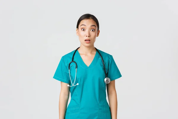 Covid-19, pracownicy służby zdrowia, koncepcja pandemii. Imponująca i zaskoczona azjatycka pielęgniarka w fartuchu opuszcza szczękę i gapi się na niemowę aparatu, wyglądając zdumiewająco na białym tle — Zdjęcie stockowe