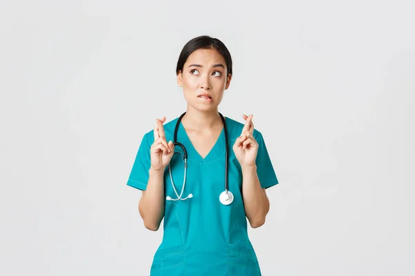 Covid-19, sağlık çalışanları, salgın konsepti. Umut dolu Asyalı kadın stajyer doktor haberleri bekliyor. Sol üst köşeye bakıp dudak ısırıyor. Dua ediyor. — Stok fotoğraf