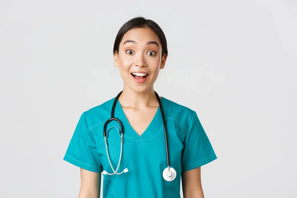 Healthcare workers, preventing virus, quarantine campaign concept. Happy and excited asian female doctor, physician in scrubs look amazed, hear awesome news, white background — Stock Photo, Image