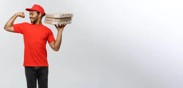 Lieferkonzept - Porträt eines starken afrikanisch-amerikanischen Zustellers, der seine Muskeln mit Pizzakartonverpackungen zeigt. isoliert auf grauem Studiohintergrund. Kopierraum. — Stockfoto