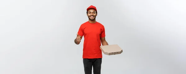 Koncepcja dostawy - portret szczęśliwy African American człowiek dostawy gospodarstwa pizza box pakiet i Wyświetlono thumps. Na białym tle na studio szary tło. Miejsce. — Zdjęcie stockowe
