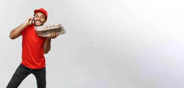 Concepto de entrega - Retrato del guapo repartidor de pizza afroamericana al teléfono con el cliente. Aislado en Grey studio Background. Copiar espacio . —  Fotos de Stock