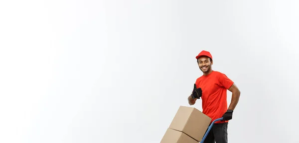 Conceito de entrega - Retrato de belo entregador afro-americano ou mensageiro empurrando caminhão de mão com pilha de caixas. Isolado no estúdio Grey Background. Espaço de cópia . — Fotografia de Stock