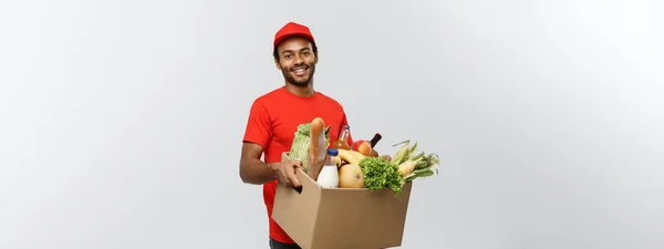 Delivery Concept - Schöner afroamerikanischer Zusteller, der Päckchen mit Lebensmitteln und Getränken aus dem Geschäft trägt. Isoliert auf grauem Studiohintergrund. Kopierraum. — Stockfoto