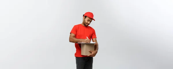 Concepto de entrega - Retrato del guapo repartidor afroamericano o mensajero escribiendo en un documento de pedido. Aislado en Grey studio Background. Copiar espacio . —  Fotos de Stock