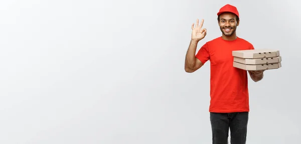 Concepto de entrega: retrato del guapo repartidor de pizza afroamericana haciendo una señal aceptable con los dedos. Aislado en Grey studio Background. Copiar espacio . —  Fotos de Stock