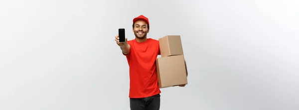 Conceito de entrega - Retrato de entregador afro-americano bonito ou mensageiro com caixa mostrando telefone celular em você para verificar o pedido. Isolado no estúdio Grey Background. Espaço de cópia . — Fotografia de Stock