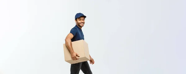 Concepto de entrega - Retrato del hombre de entrega afroamericano feliz en tela azul caminando para enviar un paquete de caja al cliente. Aislado en Grey studio Background. Copiar espacio . —  Fotos de Stock