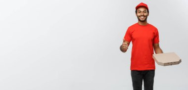 Teslimat kavram - bir pizza kutusu paket tutarak ve thumps gösterilmesini mutlu Afrika kökenli Amerikalı teslimatçı portresi. Arka plan gri studio izole. Kopya alanı.