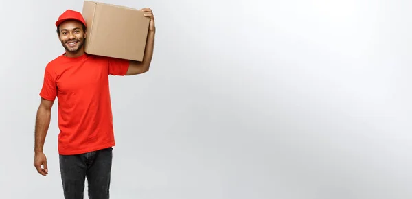 Delivery Concept - Portrait of Happy African American delivery man in red cloth holding a box package. Isolated on Grey studio Background. Copy Space. — Stock Photo, Image