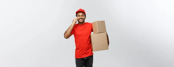 Concepto de entrega - Retrato del guapo repartidor afroamericano o mensajero con teléfono de llamada de caja al cliente. Aislado en Grey studio Background. Copiar espacio . —  Fotos de Stock