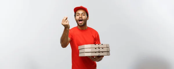 Leverans koncept - porträtt av Happy African American leverans man visar läckra gest för hand med holding lådor för pizza paketet. Isolerad på grå studio bakgrund. Kopiera utrymme. — Stockfoto