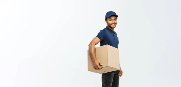 Concepto de entrega - Retrato del hombre de entrega afroamericano feliz en tela azul caminando para enviar un paquete de caja al cliente. Aislado en Grey studio Background. Copiar espacio . —  Fotos de Stock