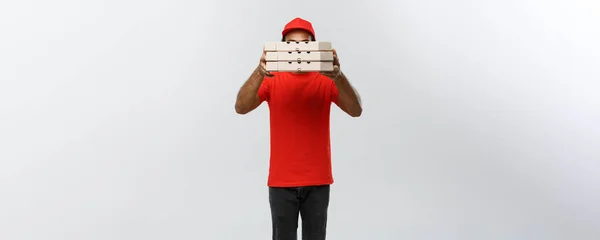 Lieferkonzept - Porträt eines gut aussehenden afrikanisch-amerikanischen Pizzaboten, der sich hinter Pizzakartons versteckt. isoliert auf grauem Studiohintergrund. Kopierraum. — Stockfoto