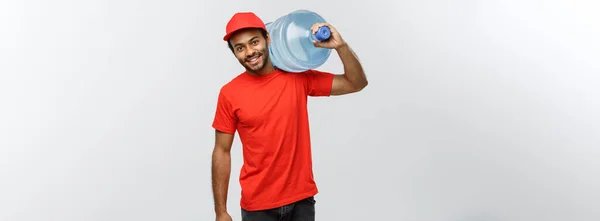 Leverans koncept - stilig African American leverans man hålla vattentanken. Isolerad på grå studio bakgrund. Kopiera utrymme. — Stockfoto