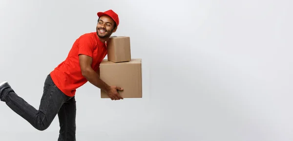 Conceito de entrega - Bonito afro-americano entrega homem corrida para entregar um pacote para o cliente. Isolado no estúdio Grey Background. Espaço de cópia . — Fotografia de Stock