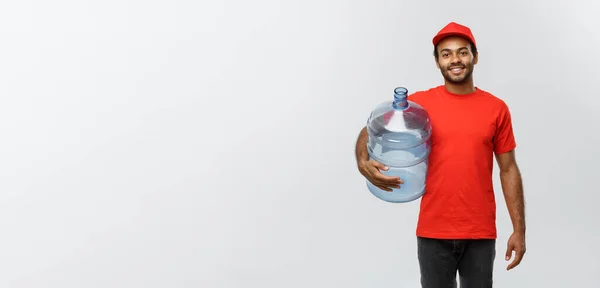 Concepto de entrega - Guapo repartidor afroamericano que sostiene el tanque de agua. Aislado en Grey studio Background. Copiar espacio . —  Fotos de Stock