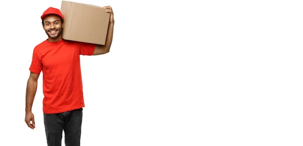 Conceito de entrega - Retrato de homem de entrega afro-americano feliz em pano vermelho segurando um pacote de caixa. Isolado no estúdio branco Background. Espaço de cópia — Fotografia de Stock